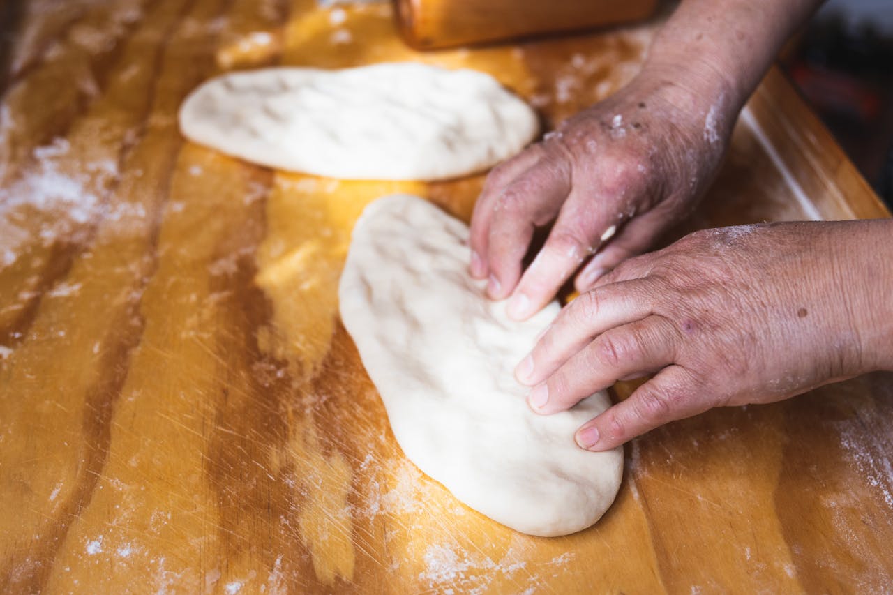 services-04 Close-up of hands kneading dough in preparation for baking on a wooden table.