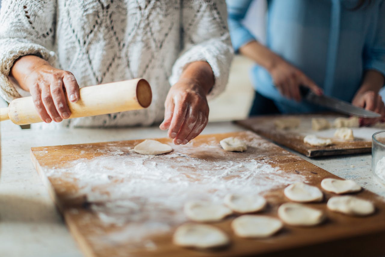 services-01 Homemade dumplings being prepared on a floured board with hands and rolling pin.