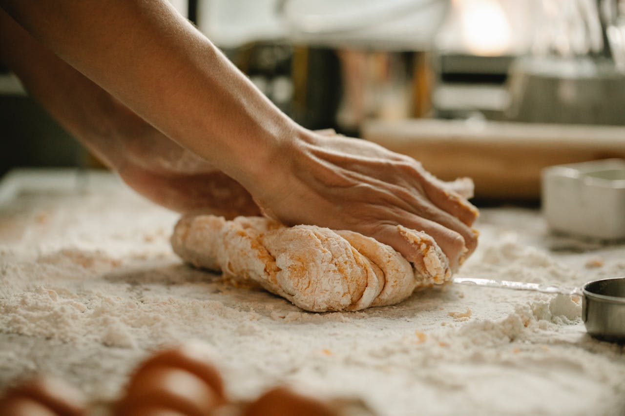 Unrecognizable woman kneading soft egg dough on table covered with flour in kitchen
