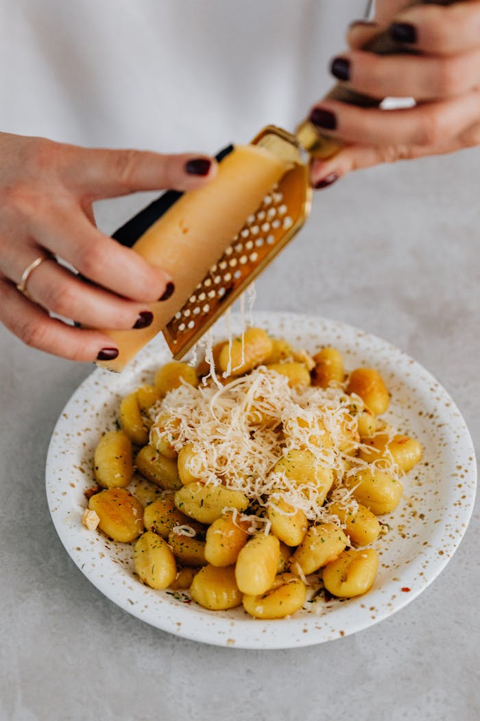 about-bg A person grates parmesan cheese over a freshly prepared gnocchi dish, Italian cuisine delight.